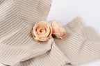 Two delicate pink roses resting on a beige fabric with black stripes.