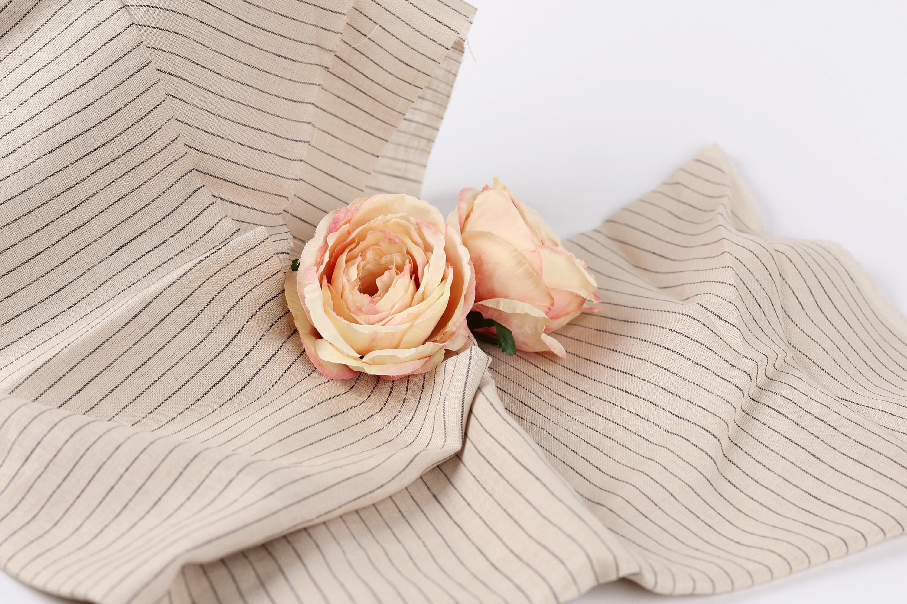 Two delicate pink roses resting on a beige fabric with black stripes.