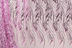 a close-up view of a fabric with a repeating pattern of pink and black sequin designs. The pattern consists of long, thin lines that create a flowing, feather-like appearance. The fabric appears to be made of a shiny, metallic material, which adds to the visual appeal of the design.