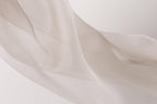 The image is a close-up of a soft, flowing fabric, possibly silk or chiffon, with a delicate texture and a light color palette.