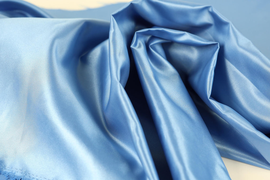 A close-up view of a blue satin fabric, with its smooth and shiny texture visible.