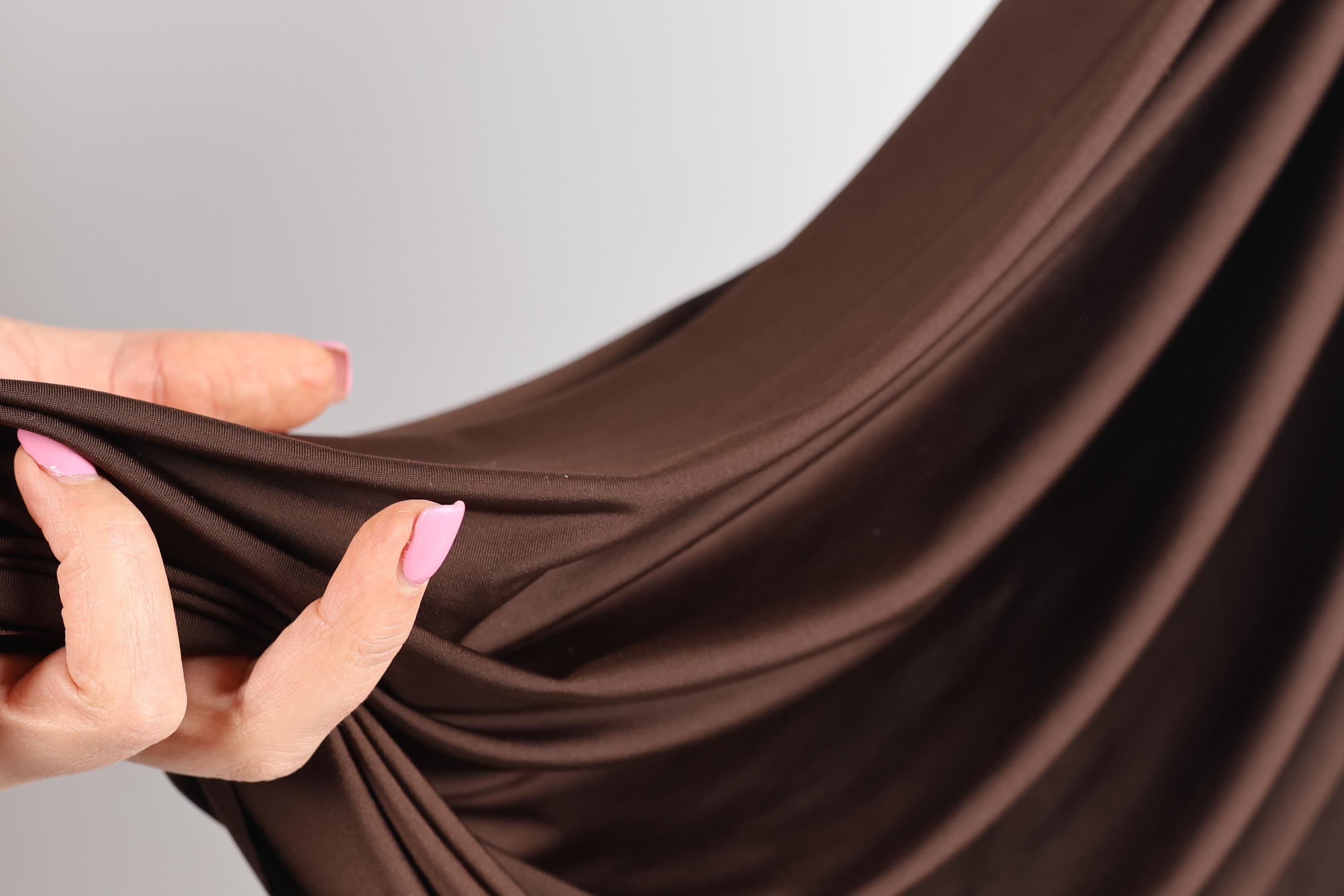 A hand with pink nail polish is holding a brown fabric, which appears to be a piece of clothing or textile.