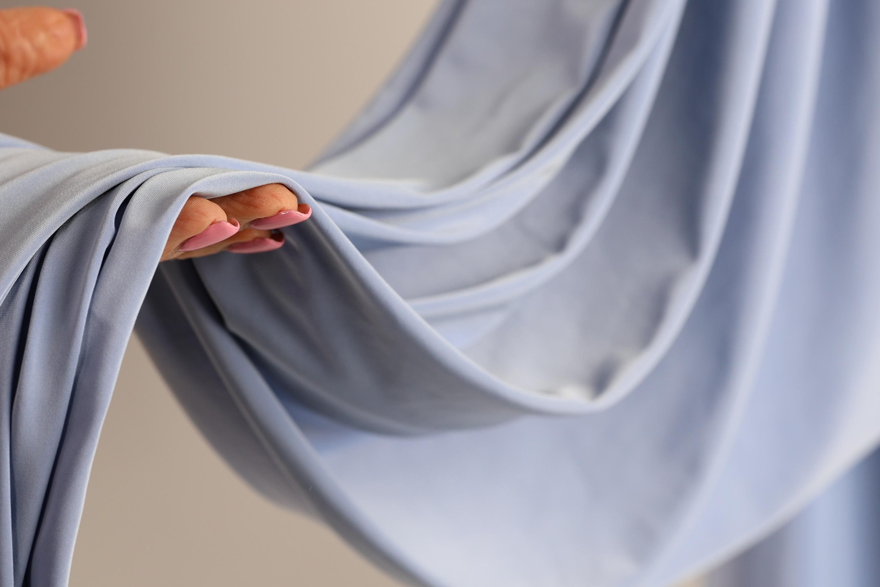 A hand with painted fingernails is holding a blue fabric, which appears to be a piece of clothing or a textile.