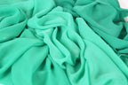 a close-up view of a fabric with a light green color, possibly mint or turquoise. The fabric appears to be crumpled and wrinkled, giving it a textured and soft appearance.