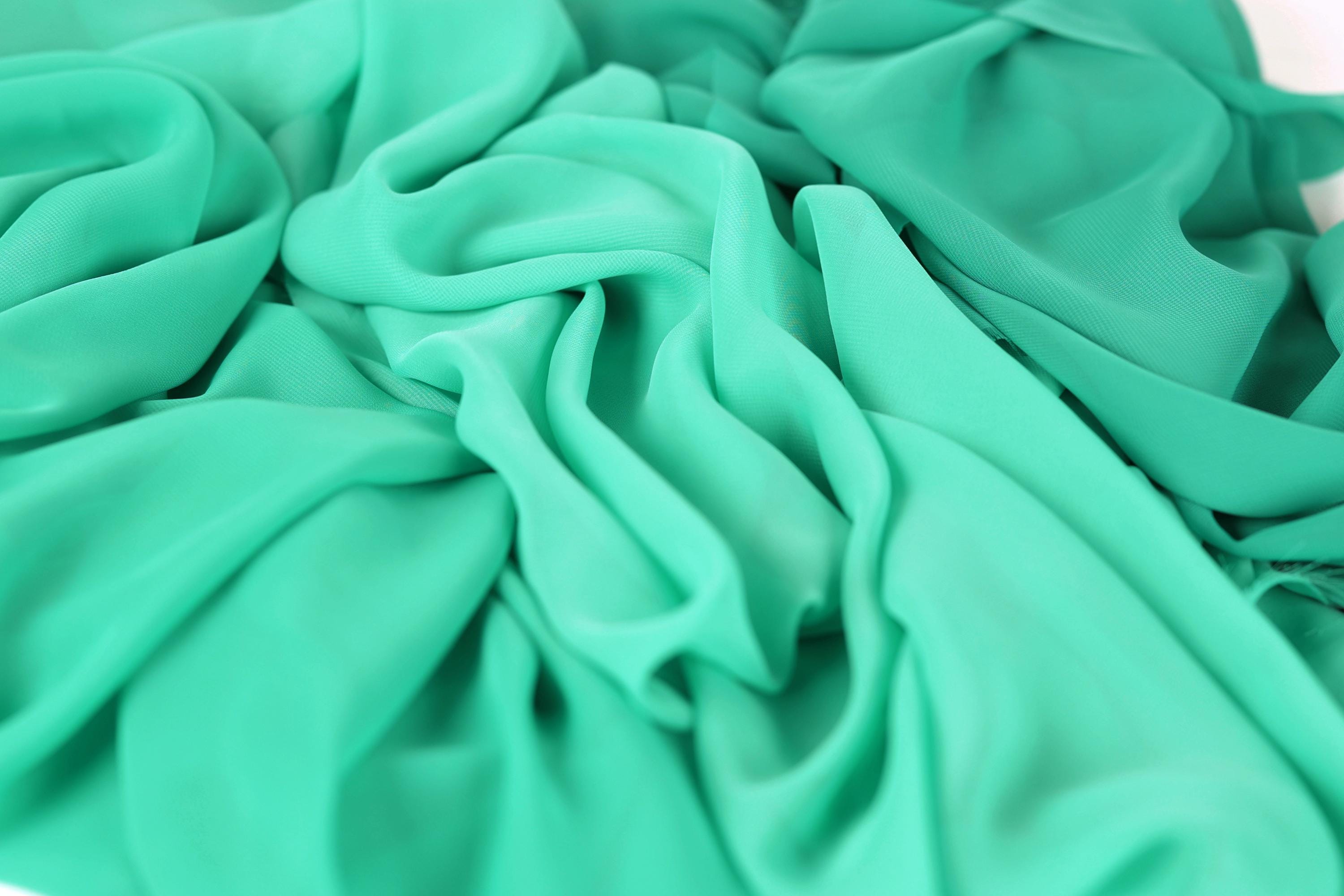 a close-up view of a fabric with a light green color, possibly mint or turquoise. The fabric appears to be crumpled and wrinkled, giving it a textured and soft appearance.