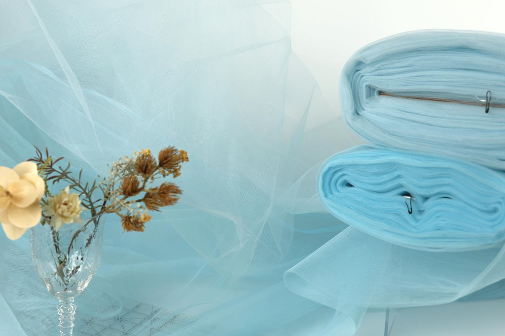 a vase with flowers, a stack of blue fabric, and a blurred background of blue fabric, creating a serene and calming atmosphere.
