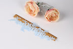 a pair of pink roses and a lace piece with blue floral patterns, placed on a white surface.
