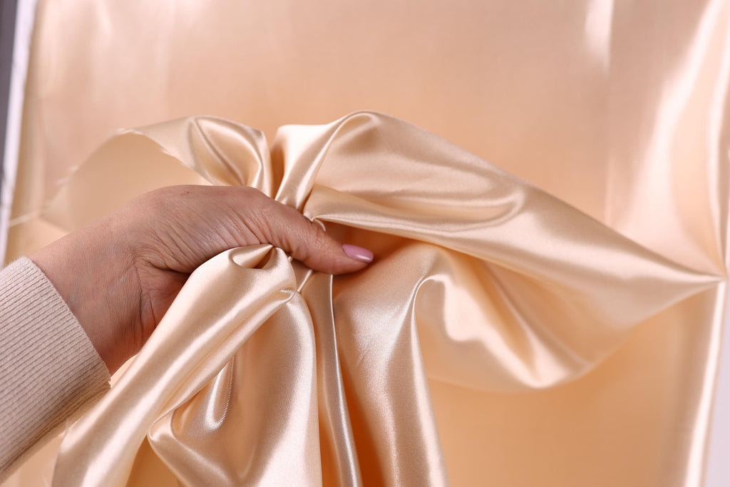 A hand is holding a piece of light pink satin fabric, which appears to be a close-up view of the material.