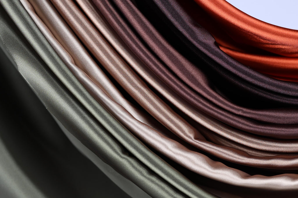 a close-up view of a collection of colorful satin fabric, with a gradient of colors ranging from light to dark brown.