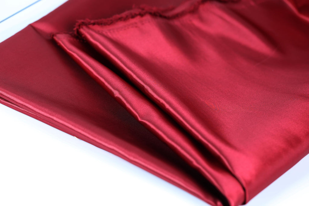 A close-up view of a red satin fabric, with a slightly wrinkled texture and a shiny appearance.