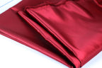 A close-up view of a red satin fabric, with a slightly wrinkled texture and a shiny appearance.