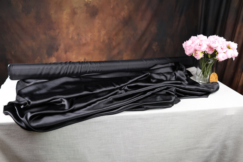 a black satin fabric, a vase of pink flowers, and a white tablecloth, all arranged on a table.