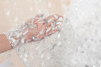 A hand holding a delicate, white lace fabric with silver sequin details.