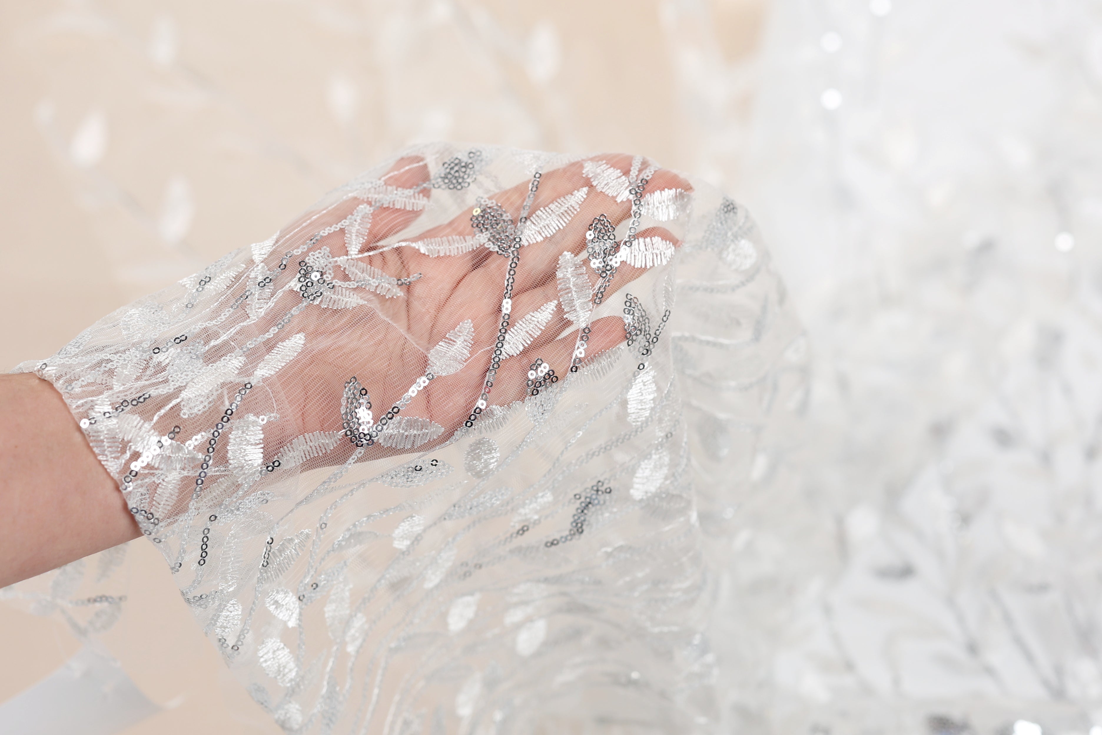 A hand holding a delicate, white lace fabric with silver sequin details.