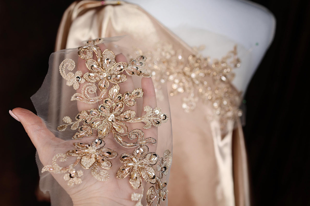 A hand holding a piece of fabric with intricate gold embroidery on it.