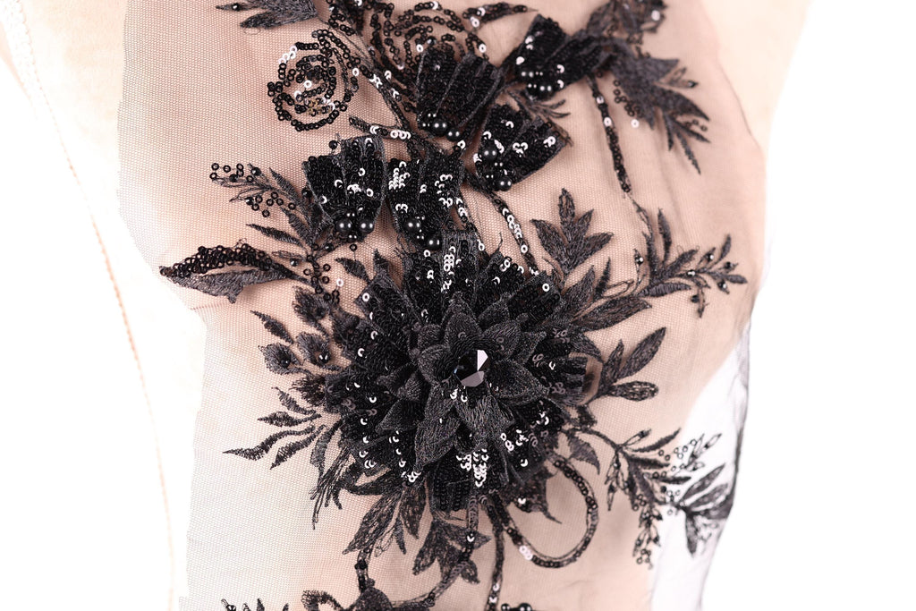 a close-up view of a delicate, intricate black lace design with a floral pattern. The lace appears to be embellished with sequins, giving it a shiny, elegant appearance.