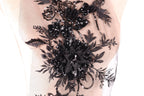 a close-up view of a delicate, intricate black lace design with a floral pattern. The lace appears to be embellished with sequins, giving it a shiny, elegant appearance.