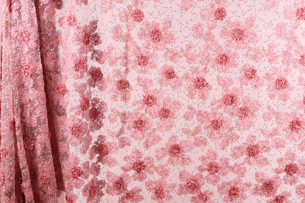 a close-up view of a fabric with a pink floral pattern. The fabric appears to be made of a sheer material, with a repeating pattern of pink flowers and leaves. The fabric is displayed in a vertical orientation, with the left side of the fabric partially visible.