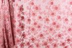a close-up view of a fabric with a pink floral pattern. The fabric appears to be made of a sheer material, with a repeating pattern of pink flowers and leaves. The fabric is displayed in a vertical orientation, with the left side of the fabric partially visible.