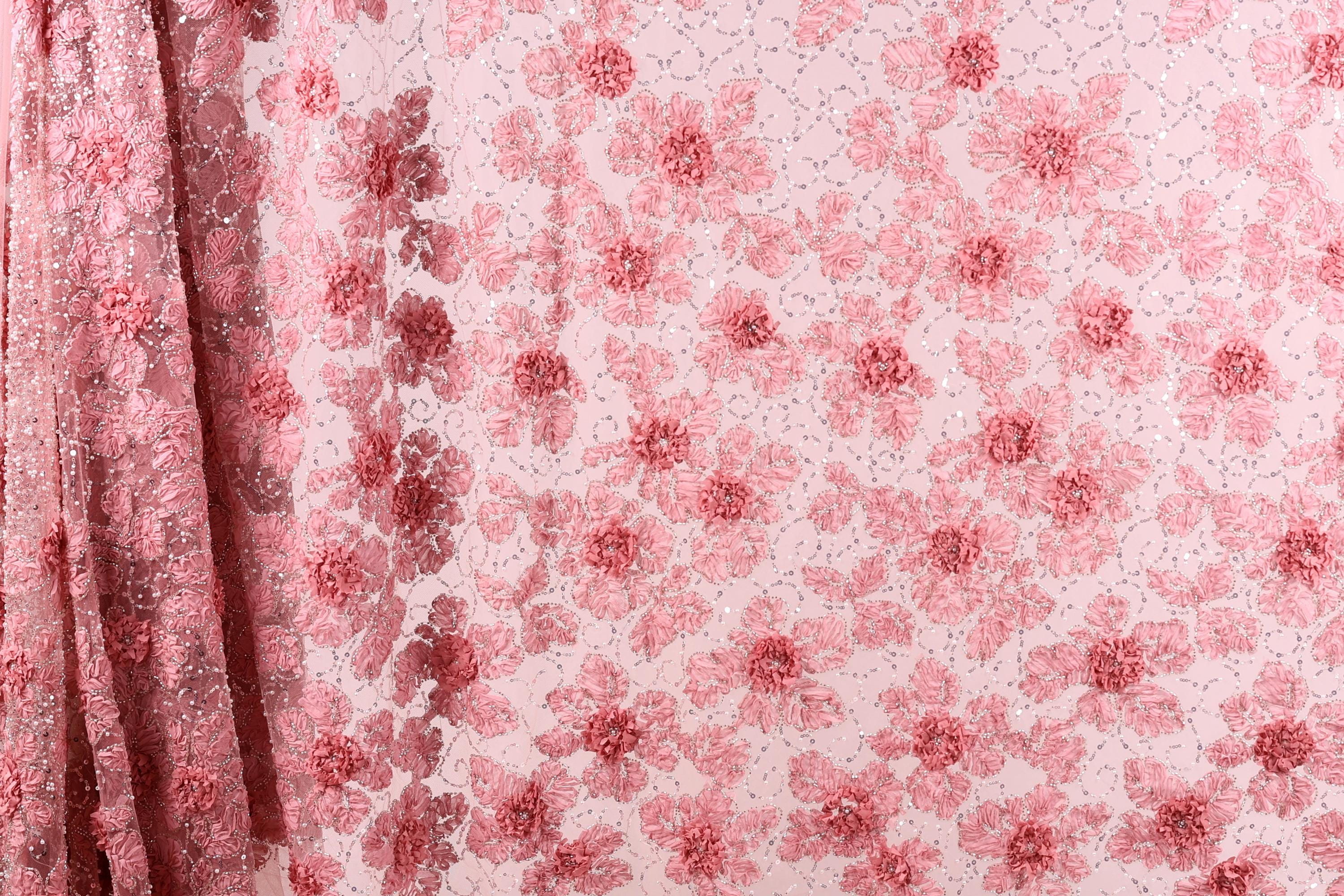 a close-up view of a fabric with a pink floral pattern. The fabric appears to be made of a sheer material, with a repeating pattern of pink flowers and leaves. The fabric is displayed in a vertical orientation, with the left side of the fabric partially visible.