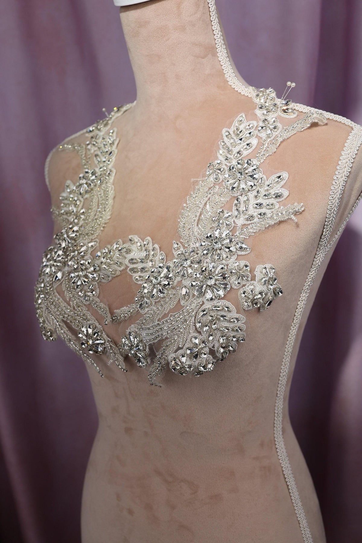 A mannequin wearing a dress with a lace bodice adorned with intricate silver and white embellishments, including floral and leaf designs.