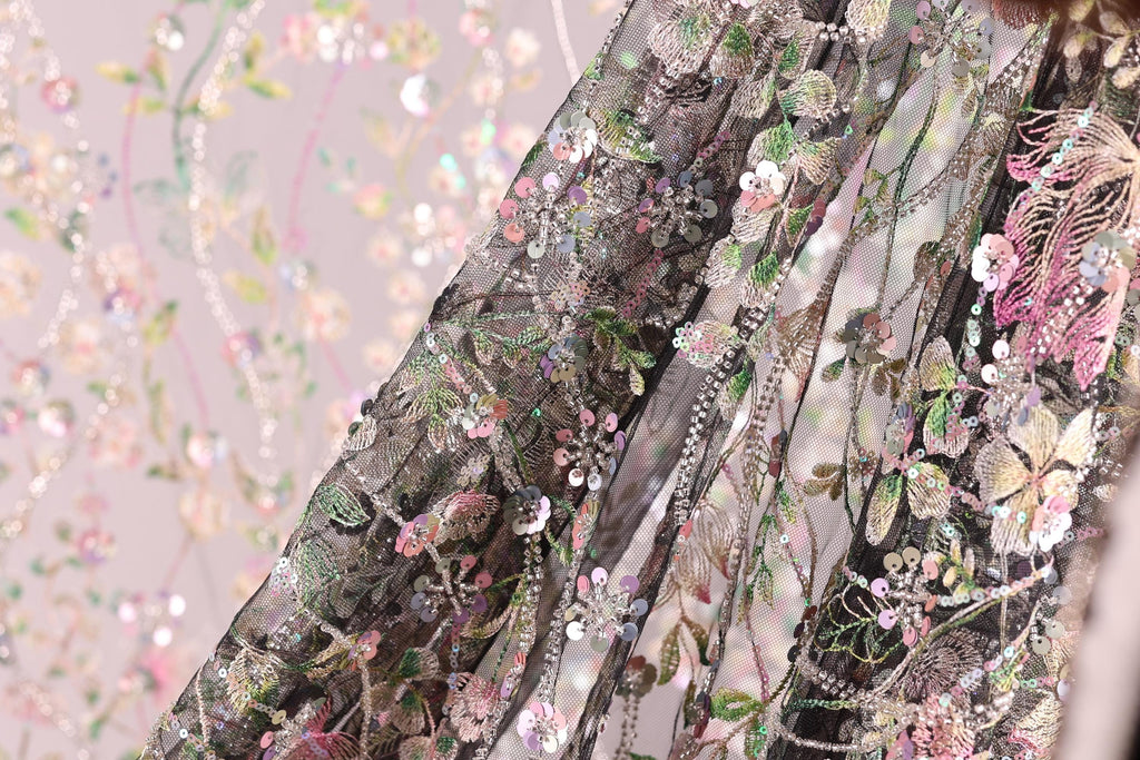 a close-up view of a fabric with a floral pattern, featuring a mix of pink, green, and white colors. The fabric appears to be made of a sheer material, with a delicate and intricate design.