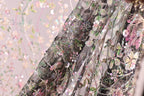 a close-up view of a fabric with a floral pattern, featuring a mix of pink, green, and white colors. The fabric appears to be made of a sheer material, with a delicate and intricate design.