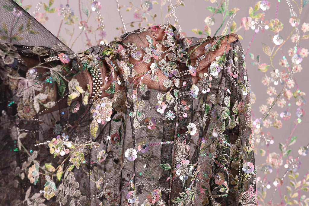 a close-up view of a delicate, intricately embroidered fabric with a floral pattern. The fabric appears to be a sheer material, with a black background that contrasts with the colorful floral design. The image is a close-up shot of the fabric, showcasing its detailed embroidery and the intricate patterns created by the flowers and leaves.