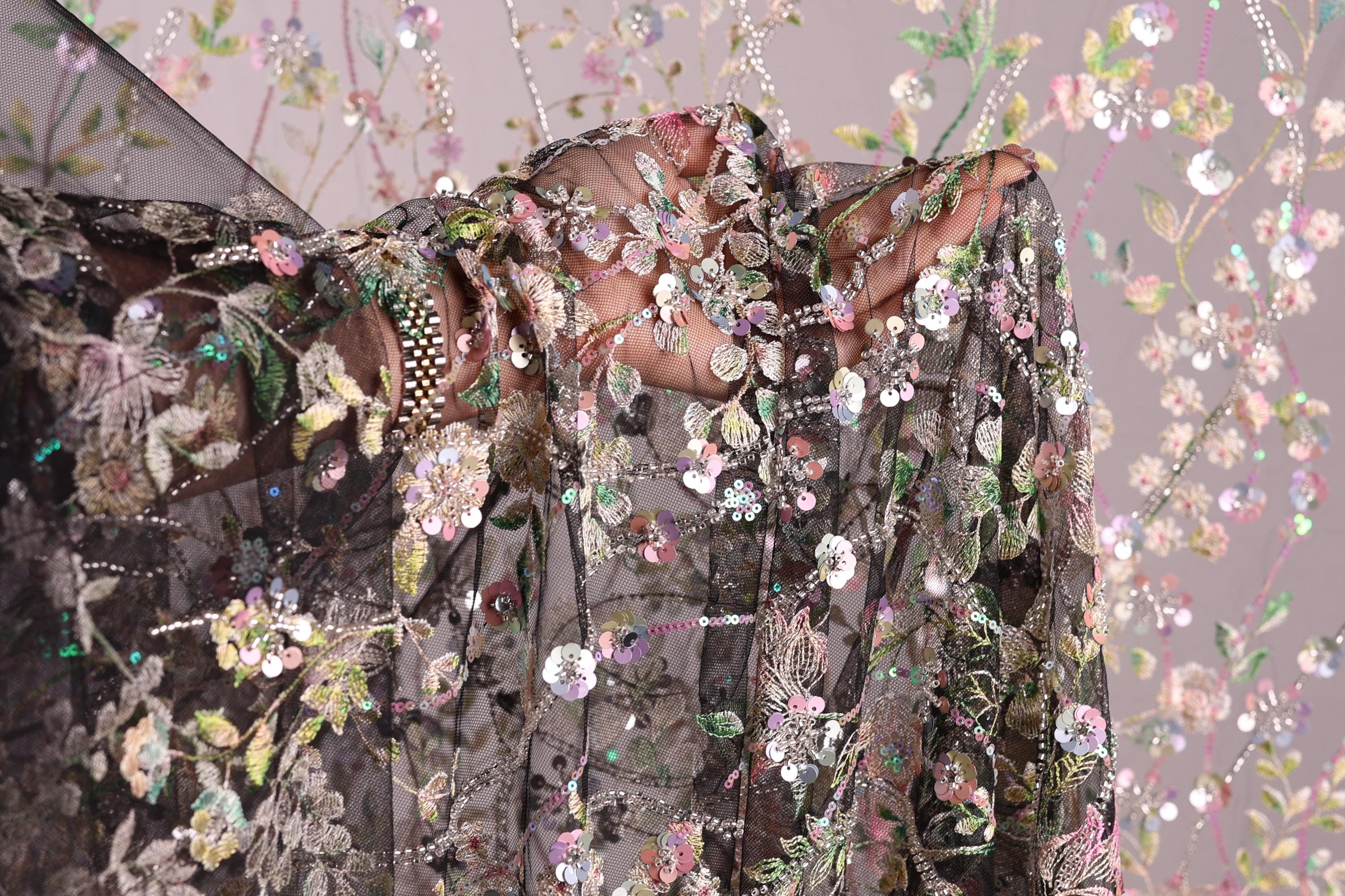 a close-up view of a delicate, intricately embroidered fabric with a floral pattern. The fabric appears to be a sheer material, with a black background that contrasts with the colorful floral design. The image is a close-up shot of the fabric, showcasing its detailed embroidery and the intricate patterns created by the flowers and leaves.