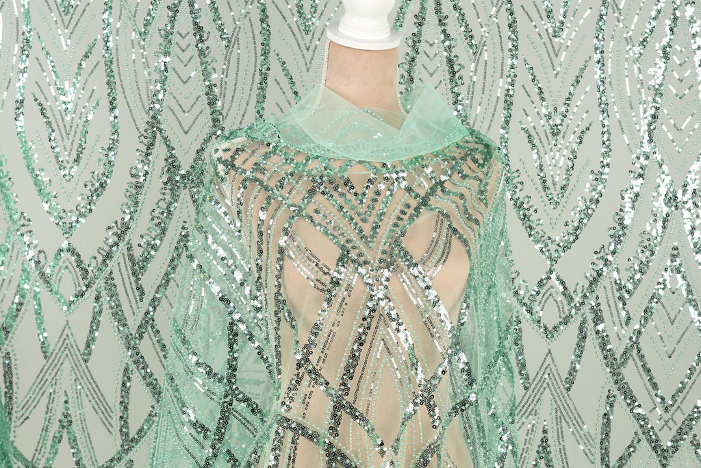a mannequin wearing a green sequin dress with a sheer overlay. The dress has a pattern of green and silver sequins, creating a visually striking and intricate design.
