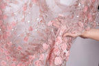 A hand is holding a piece of fabric with a delicate floral pattern of pink roses and leaves.