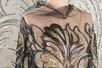 a mannequin wearing a dress with a sheer, sheer-like fabric and a floral pattern. The dress is adorned with sequins and beads, giving it a glamorous and elegant appearance.