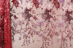 a close-up view of a fabric with a floral pattern in shades of red and pink. The fabric appears to be made of sequin material, creating a visually striking and intricate design.