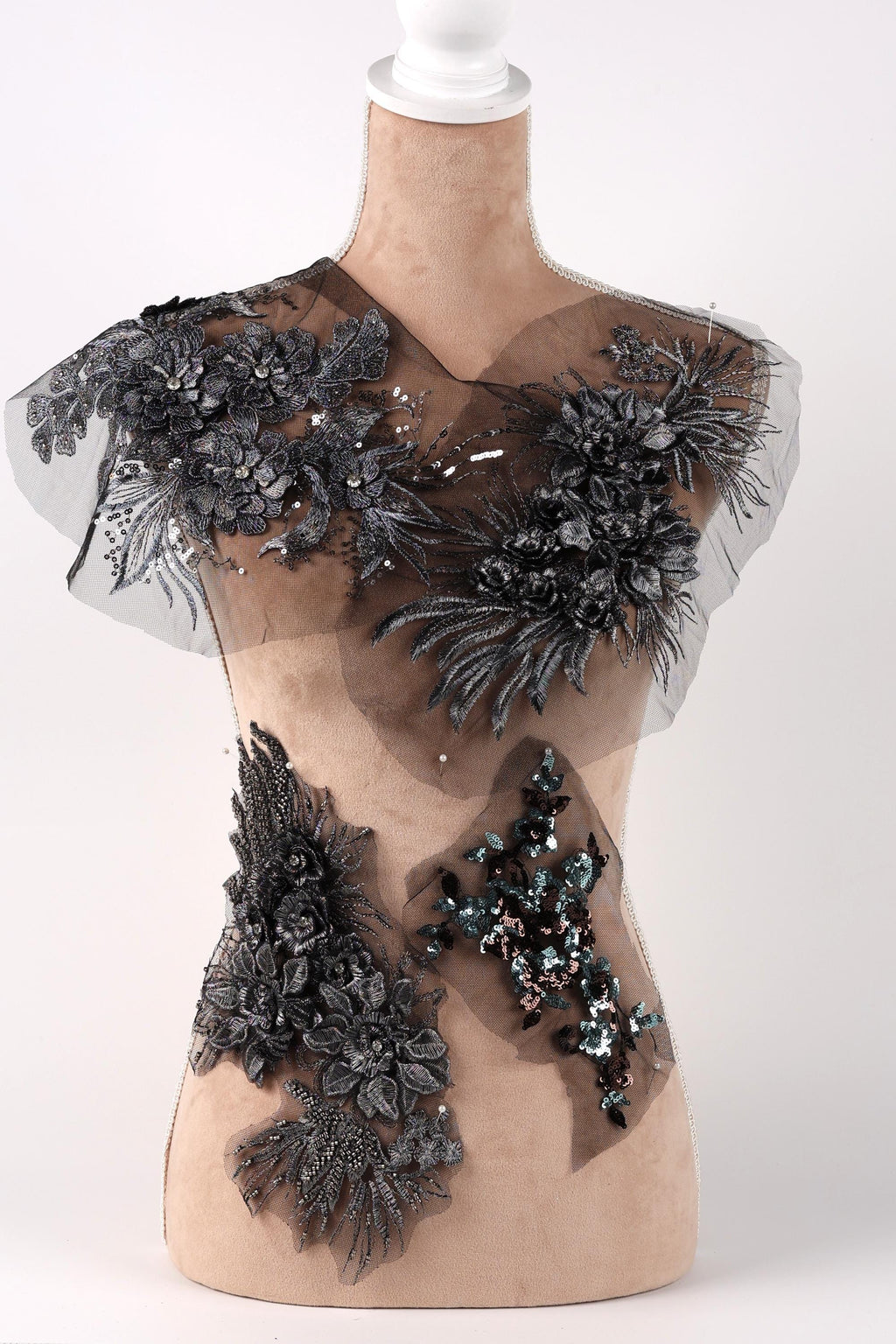 A mannequin with a beige body and a white head, wearing a dress with intricate black and gray floral and sequin embellishments.