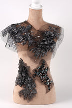 A mannequin with a beige body and a white head, wearing a dress with intricate black and gray floral and sequin embellishments.
