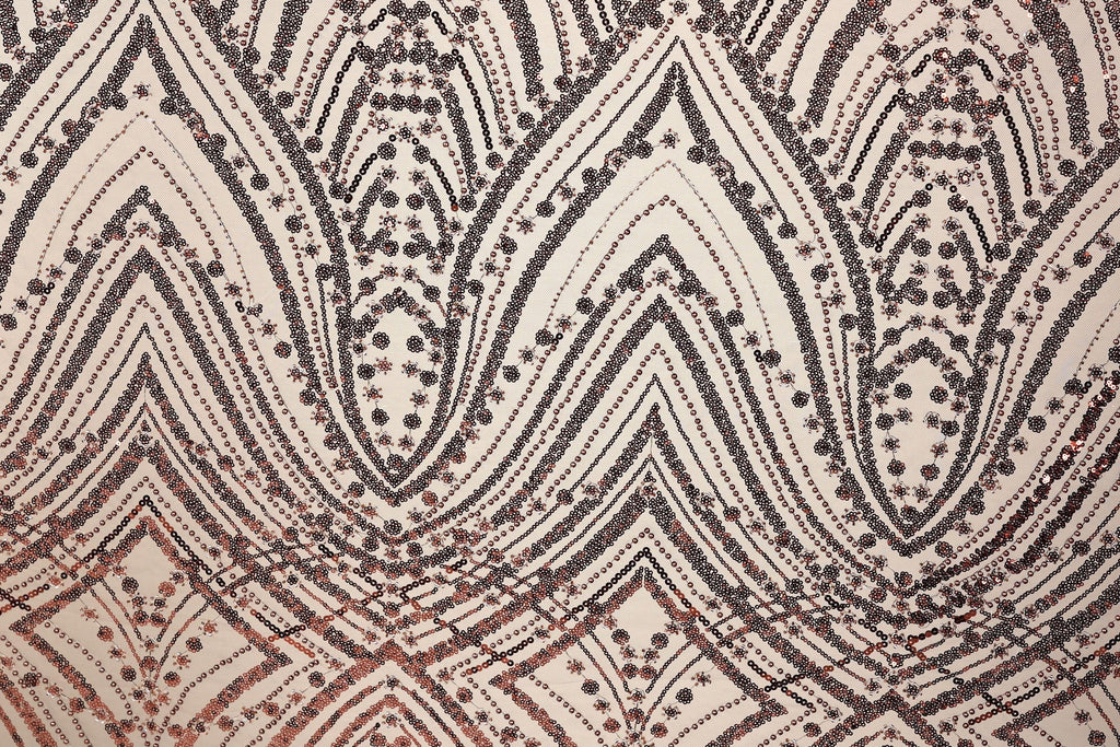 a close-up view of a fabric with a repeating pattern of black and brown geometric shapes, including triangles, diamonds, and other abstract designs. The pattern appears to be a decorative textile or fabric with a metallic or sequined appearance.