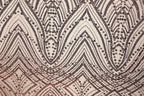 a close-up view of a fabric with a repeating pattern of black and brown geometric shapes, including triangles, diamonds, and other abstract designs. The pattern appears to be a decorative textile or fabric with a metallic or sequined appearance.