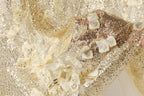 The image is a close-up of a fabric with a gold and white color scheme, featuring a floral pattern and sequins.