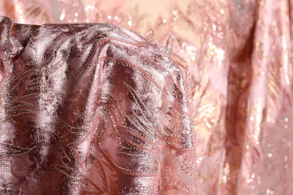 a close-up view of a fabric with a pink and gold sequined pattern, featuring a delicate and intricate design.