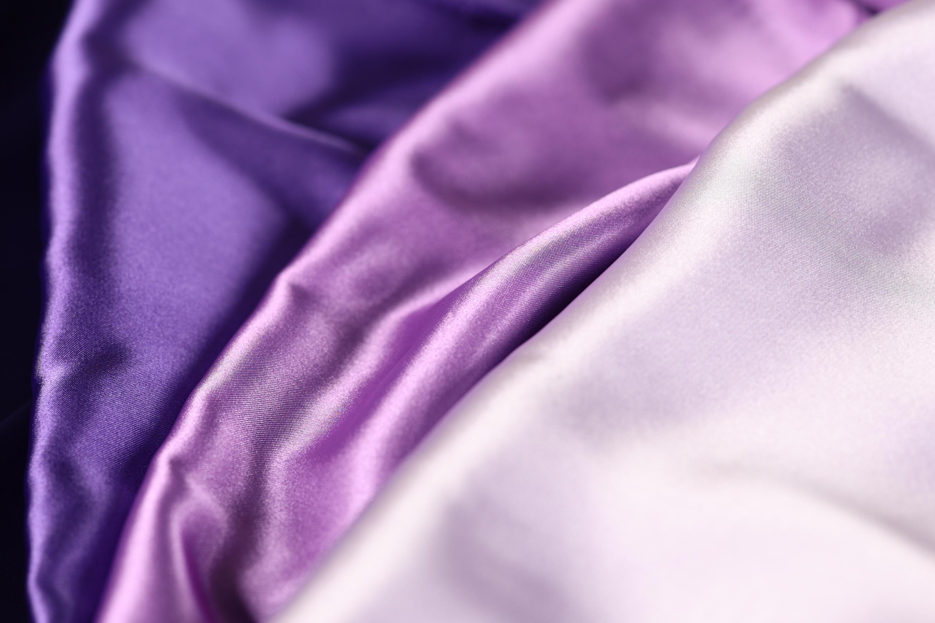a close-up view of three different colored satin fabrics, with the colors being purple, lavender, and white.