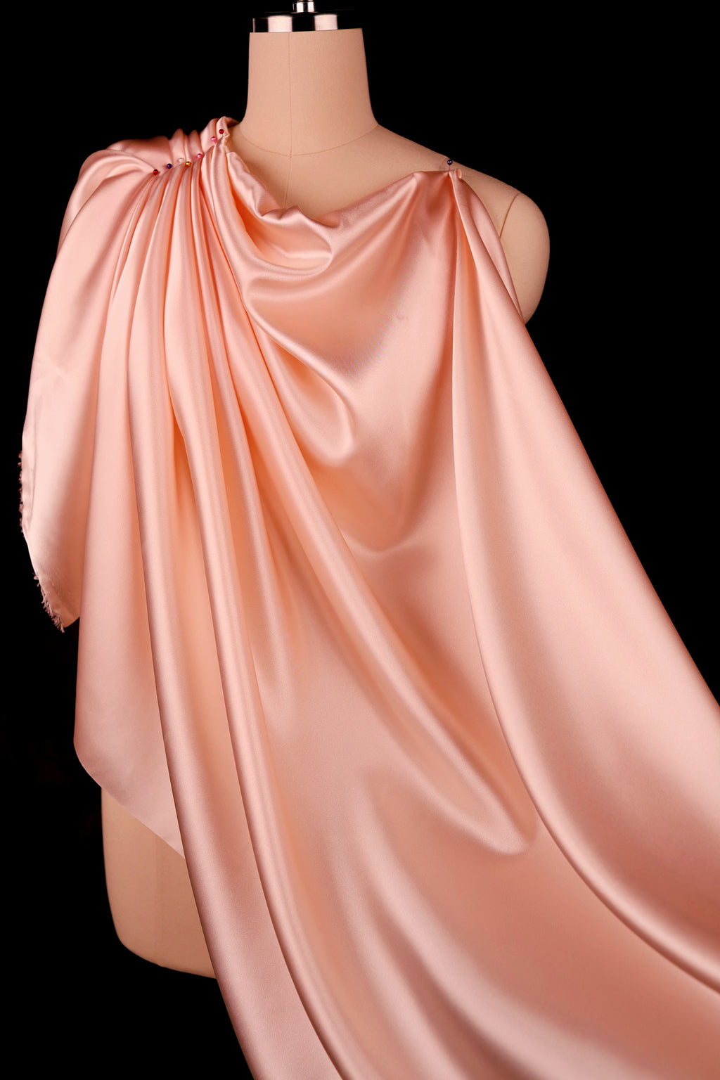 A mannequin wearing a flowing, draped peach-colored satin fabric.