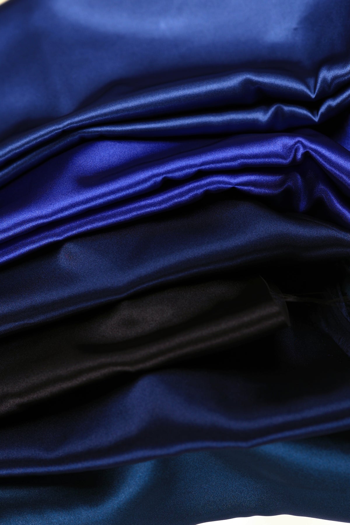 The image is a close-up of a pile of various colored satin fabric, including shades of blue, black, and purple.