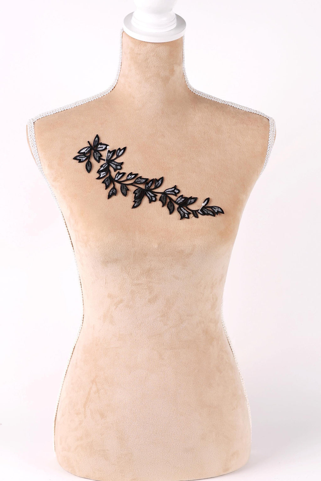 A mannequin with a beige body and a black leaf embroidered on its chest.