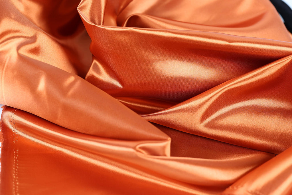 The image is a close-up of a crumpled orange satin fabric, with a textured and shiny appearance.