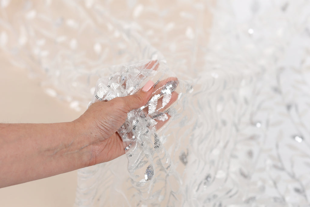 A hand holding a piece of sequin fabric against a blurred background.