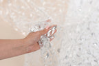 A hand holding a piece of sequin fabric against a blurred background.