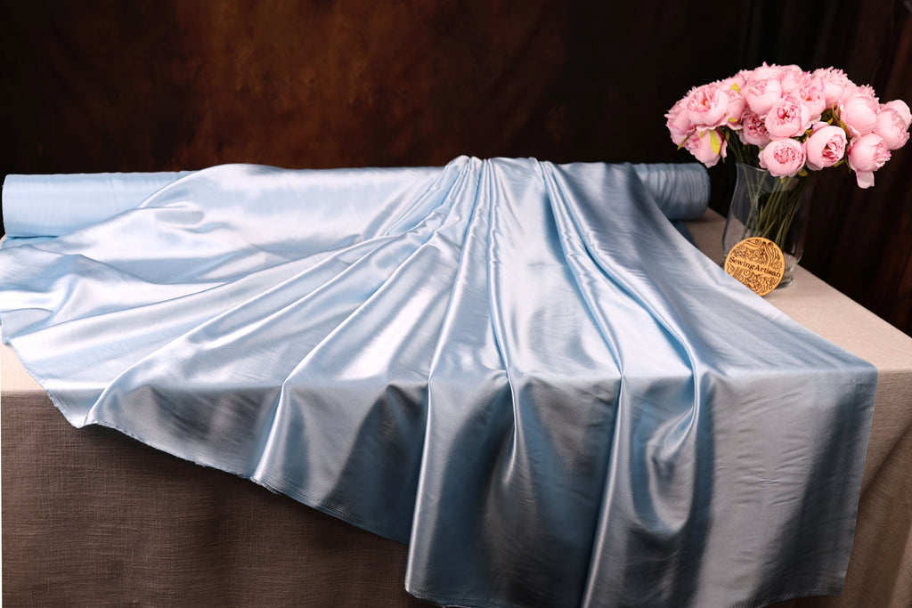 a blue satin fabric draped over a table, with a vase of pink roses placed next to it.