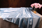 a blue satin fabric draped over a table, with a vase of pink roses placed next to it.