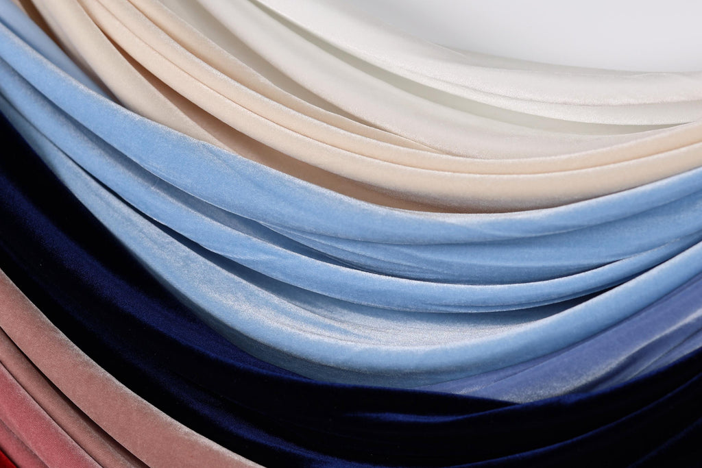 A close-up image of various colored velvet fabric swatches, including blue, pink, and white, arranged in a layered and textured manner.