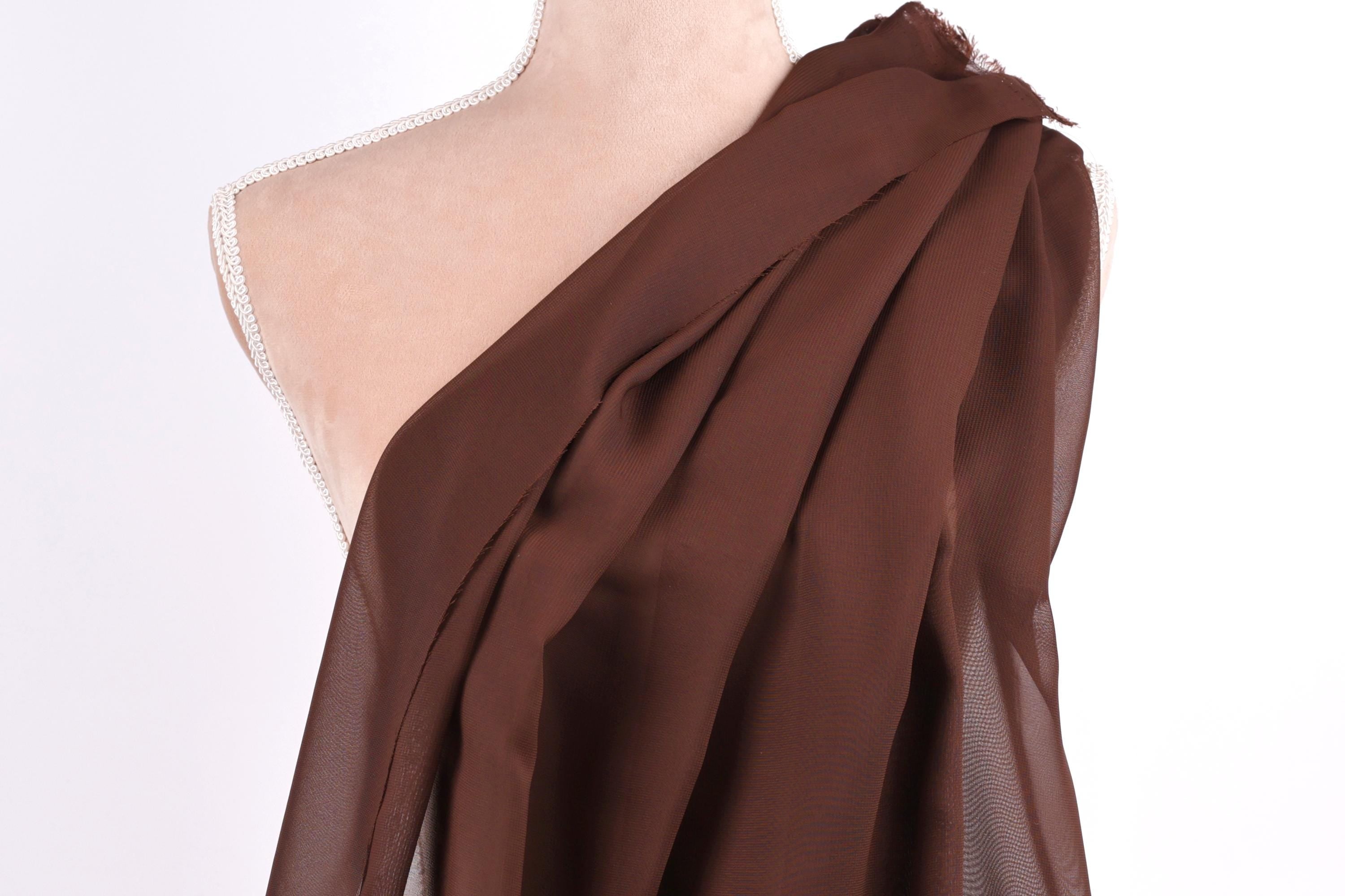 A mannequin wearing a brown draped fabric draped over its shoulder.